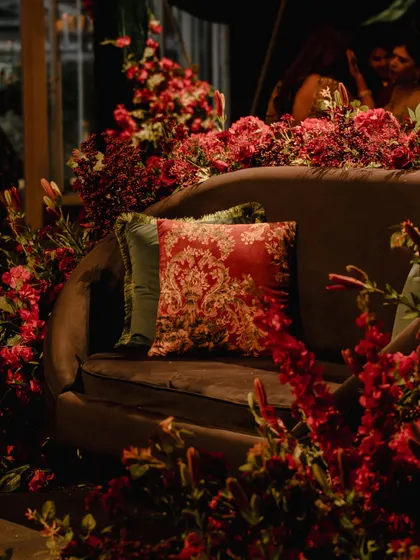 For this sangeet, I designed a cozy yet luxurious seating area by surrounding a plush sofa with a forest of red flowers. The baroque-style cushion adds a touch of old-world romance to the modern setup.