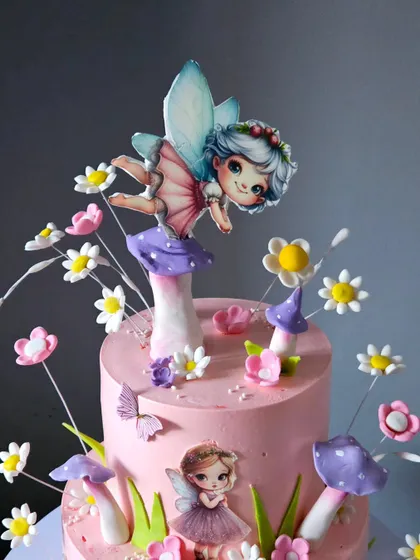 A close-up of the top of the two-tiered fairy cake. This view shows the main fairy topper, surrounded by whimsical, wired sugar flowers that seem to dance in the air.
