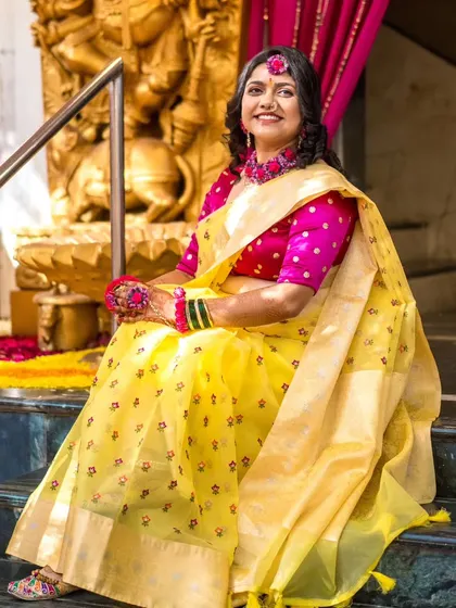 A lovely portrait of a bride at her Haldi ceremony, dressed in a yellow saree with floral jewelry, seated in a traditional setting.