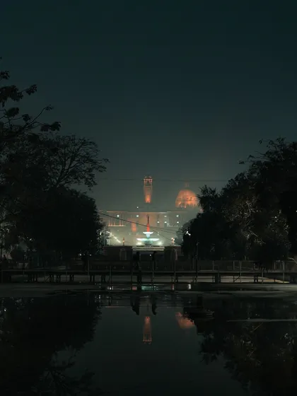 A moody, atmospheric shot of Rashtrapati Bhavan seen across the water on a foggy night in Delhi. The reflection and mist create a mysterious and dramatic feel.