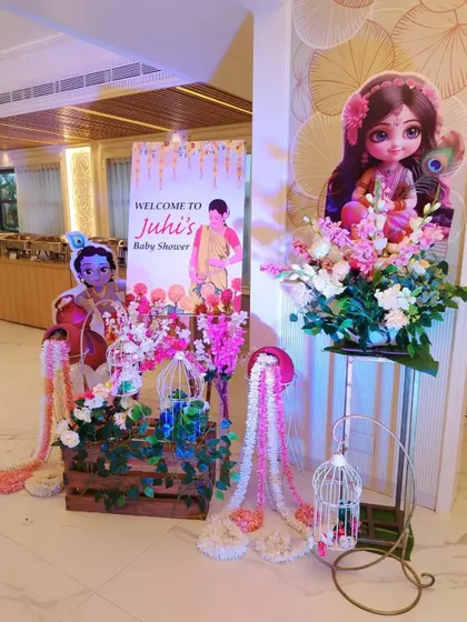 An entrance decoration for a Krishna-themed baby shower. We used a welcome standee, character cutouts, and floral arrangements with decorative birdcages to greet the guests.