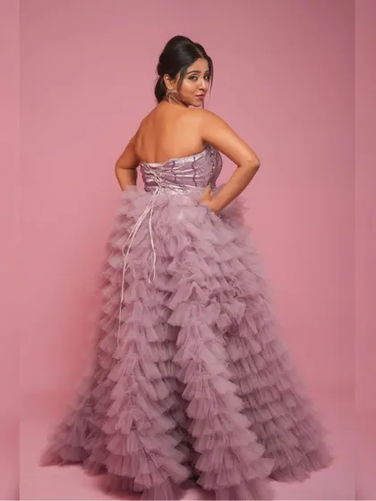 The back view of the light purple multilayer net gown, showing the corset lacing detail against a solid pink backdrop.