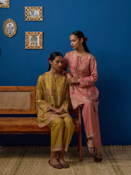 This image captures a shared, quiet moment between two models, creating a narrative for the collection. The composition feels natural and tells a story of friendship, showcasing two complementary outfits from the brand.