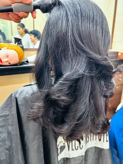 A close-up of the blow-drying process, focusing on creating smooth, curved ends to complement the layered haircut.