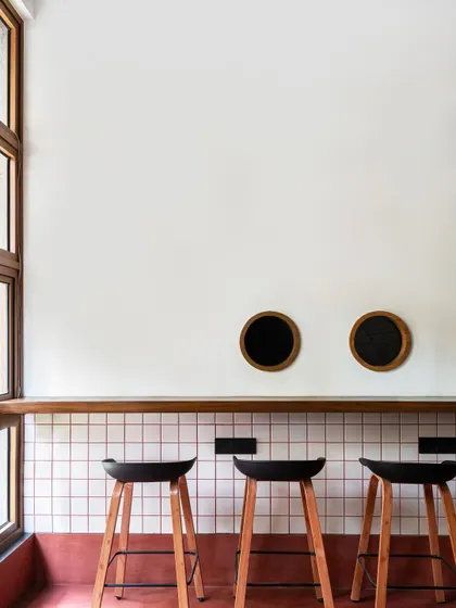 Simplicity and clean lines define the bar seating area. White grid tiles with red grouting, a simple wooden counter, and modern black stools create a look that is both retro-inspired and distinctly contemporary.