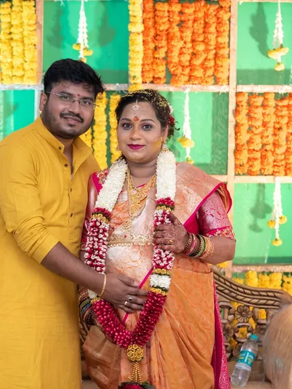 A couple poses for a portrait during their traditional baby shower ceremony, surrounded by marigold flower decorations. We are experienced in respectfully documenting traditional family functions.