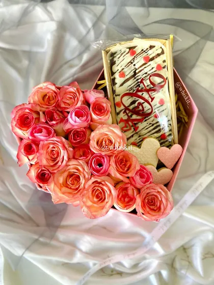 A beautiful heart-shaped box combining fresh pink roses with a "Love" brownie slab and heart-shaped cookies.
