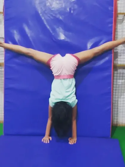 A student practices a wall-assisted split handstand, an advanced stretch that improves flexibility in the shoulders and legs.