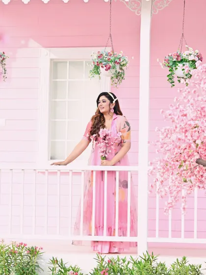 The model poses on the porch of a pink house, surrounded by flowers. This shot has a charming, storybook quality that is both sweet and fashionable.