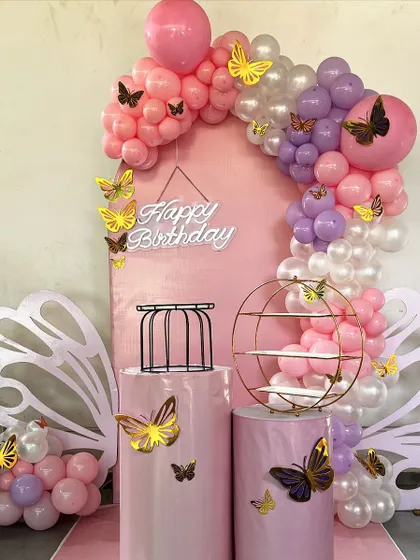 A pink and purple butterfly-themed backdrop, perfect for a first birthday. This setup includes an arched backdrop, large cutout butterfly wings for photo ops, and a "Happy Birthday" neon sign.
