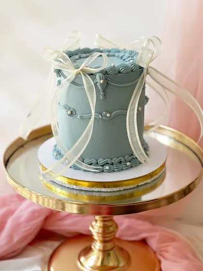 A gorgeous cake in a dusty blue-grey, featuring intricate vintage piping and delicate sheer ribbons. The pearl details add a final touch of elegance.