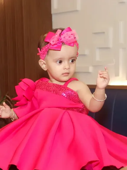 A beautiful portrait of a baby girl in a vibrant pink party dress, posing elegantly.