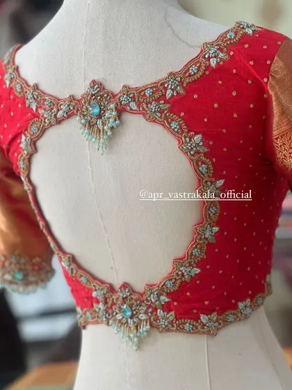 A red blouse on a mannequin, featuring a heart-shaped back cutout and light blue stone work.