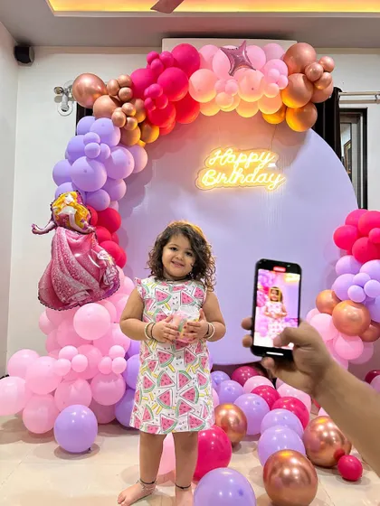 A happy birthday girl posing with our Cinderella-themed decoration. The setup features a beautiful balloon arch in shades of pink and purple.