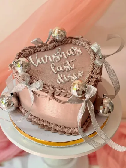 A "last disco" themed cake for a bachelorette party or birthday. This heart-shaped cake is decorated with mini disco balls and silver ribbons for a fun, retro vibe.