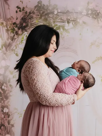 Double the joy. A beautiful mother holding her newborn twins, one in pink and one in blue, in a dreamy, floral setting.