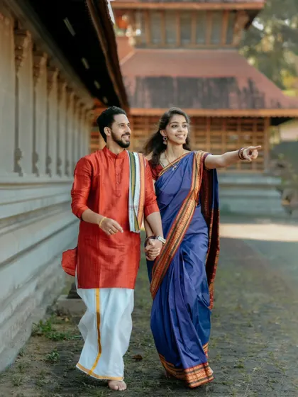 A joyful, candid shot of a couple walking hand-in-hand at a temple, with the bride pointing excitedly, capturing a moment of shared discovery.