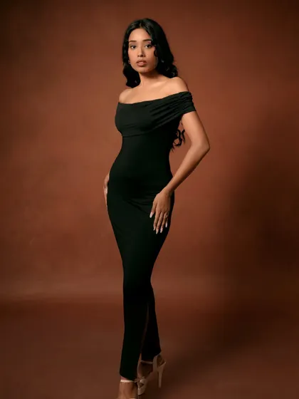 A full-length view of the elegant black dress against a warm brown background. This type of shot is essential for showing the complete look in a fashion catalog.