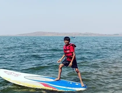 A young boy confidently stands on his paddleboard, enjoying the vast open water of Vani Vilas Sagar.