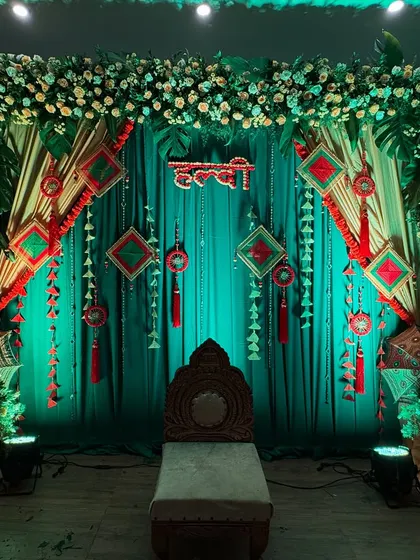 A beautiful Haldi setup with a green drape backdrop, decorated with Rajasthani-style hangings and umbrellas for a colorful and festive look.