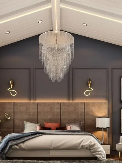 We designed this bedroom in a villa with a vaulted ceiling to maximize its grand scale. A stunning waterfall chandelier hangs from the apex, illuminating a cozy yet luxurious space with a dark accent wall and modern sconces.