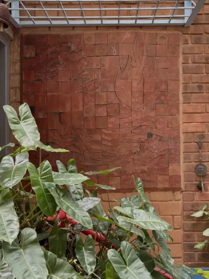 A subtle relief carving on a wall of reddish stone blocks. The artwork is integrated so seamlessly with the building material that it appears to emerge from the wall itself.