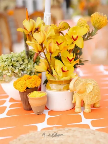 A close-up of a Haldi centerpiece, featuring yellow orchids and marigolds, with a small golden elephant figurine adding a touch of traditional Indian charm.