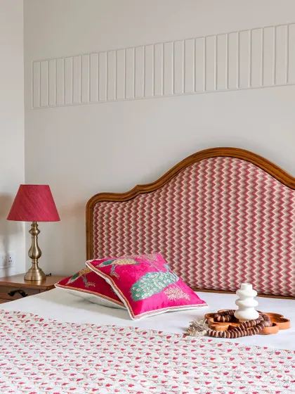 A bedroom design featuring a custom bed with a curved, wood-framed headboard upholstered in a vibrant pink chevron fabric. The wall behind features subtle vertical fluting for added texture.