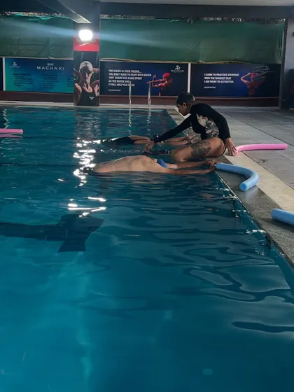 Assisting a participant in a floating Savasana using a pool noodle for support. This is the ultimate relaxation, feeling weightless and completely held by the water.