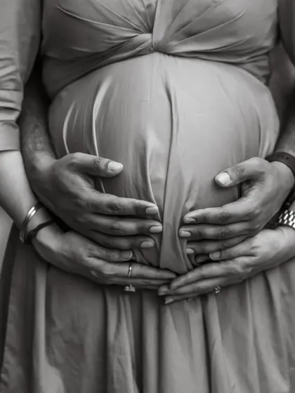 A close-up, black and white shot focusing on the couple's hands cradling the baby bump. This intimate photo symbolizes their shared love and protection for their unborn child.