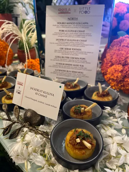 A close-up of our Jackfruit Kulliya Ki Chaat, a unique appetizer featuring charred pineapple and jackfruit. The dish label and menu in the background highlight our bespoke menu design for events.
