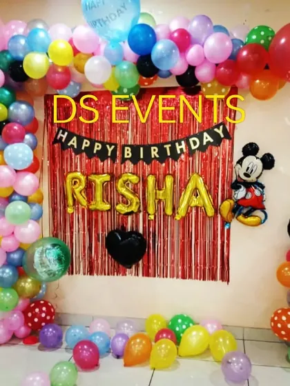 A classic and simple Mickey Mouse birthday decoration. This setup uses a red foil curtain backdrop, a "Happy Birthday" banner, and a colorful balloon frame, showing that even simple setups can be full of fun.