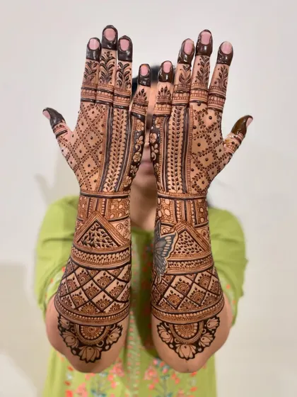 A happy bride showing off her geometric-style bridal mehendi. The design covers her hands and arms completely for a rich, traditional look.