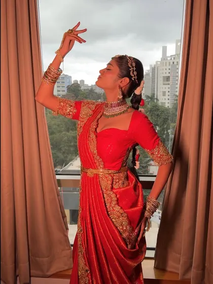 A graceful pose in the red fusion saree-lehenga. The drape allows for artistic expression and creates a beautiful silhouette against the light.