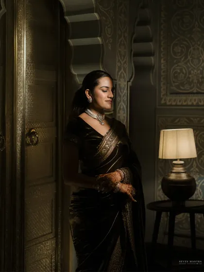 A portrait of quiet elegance. The soft lamplight and the rich textures of the room create a moody and sophisticated atmosphere for this bridal shot.