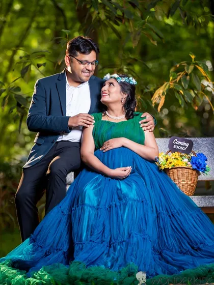 A simple park bench becomes the perfect spot for a loving portrait. The expecting mother looks stunning in a blue gown, and the "Coming Soon" sign adds a sweet, personal touch to their photo.