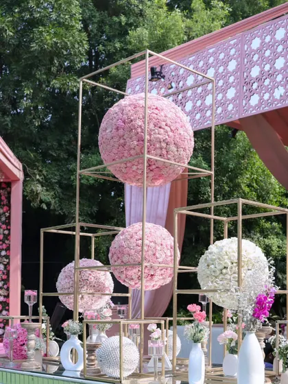 A modern and artistic floral installation. Large spheres of pink and white flowers are displayed within golden geometric frames, serving as a stunning centerpiece for a buffet table.