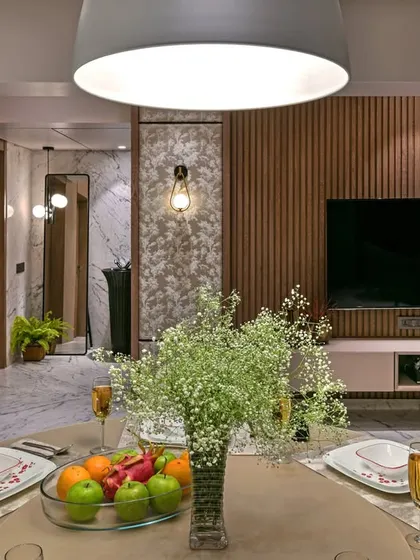 A cozy dining setup that overlooks the living area. The fluted wood paneling behind the television adds warmth and texture, creating a visual link between the dining and lounging zones.