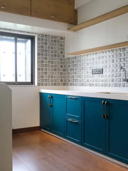 The base cabinets of this kitchen are finished in a rich teal PU paint with shaker-style doors. The design includes a mix of drawers and cabinets to accommodate different storage needs, all built from durable marine ply.