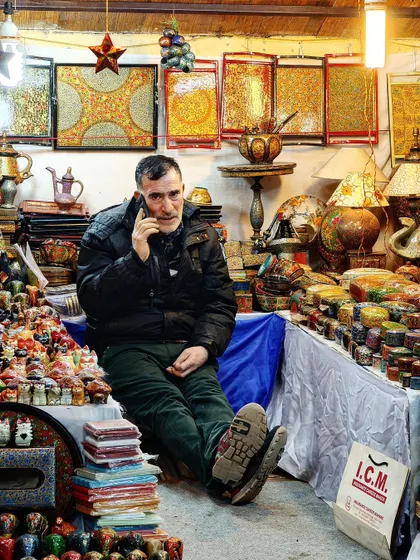 A vibrant street portrait of a shopkeeper, captured with the Realme 12 Pro+. It showcases the phone's ability to capture detail and color in a complex, real-world scene.