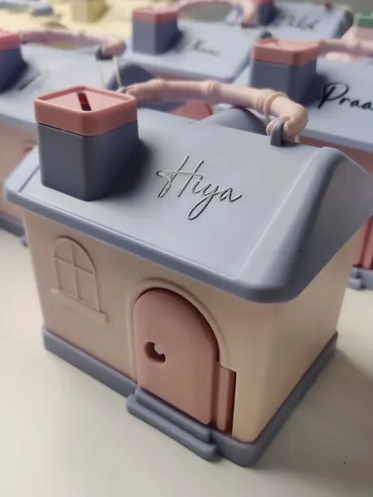 A close-up of our house-shaped piggy bank, personalized with the name "Hiya." A perfect return gift to teach kids about saving.