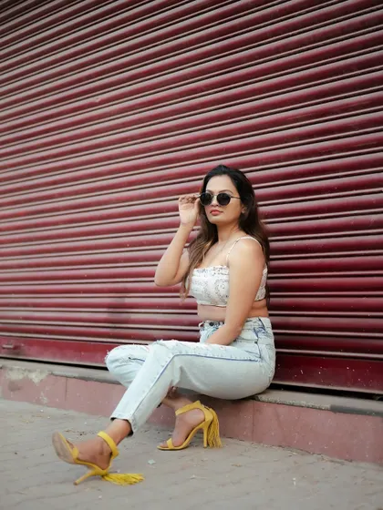 A casual portrait of a model sitting on the curb against a red shutter. The relaxed pose and urban setting create an authentic and stylish shot.
