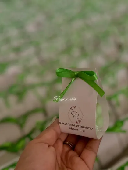 A close-up of the baby bubble candle wedding favor, showing the personalized tag with the couple's names and wedding date.