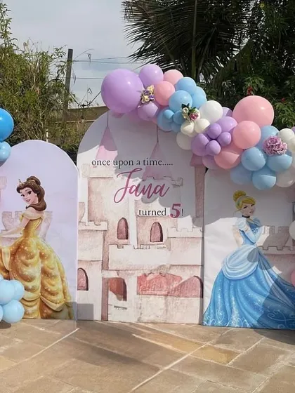 A fairytale princess theme featuring Belle and Cinderella. This outdoor setup includes three arched backdrops creating a castle-like scene, decorated with pastel balloon garlands.