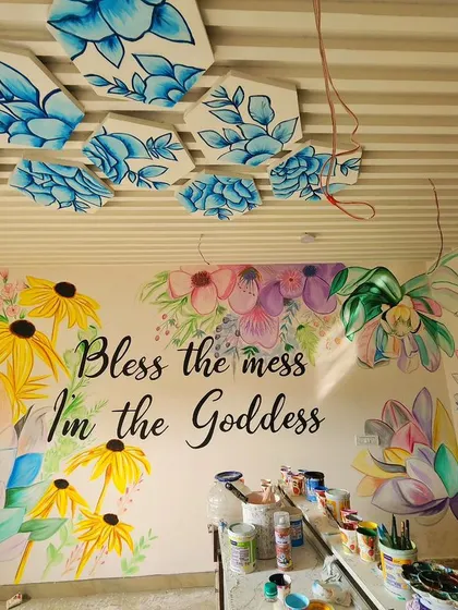 We painted this bright and cheerful floral mural for a reception area, featuring the quote "Bless the mess, I'm the Goddess." The design includes flowers painted on hexagonal panels on the ceiling.