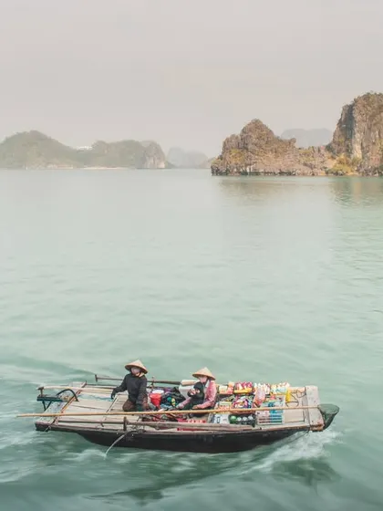 A floating shop boat is dwarfed by the majestic limestone karsts of Halong Bay in the background.