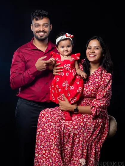 A happy family of three posing for a studio portrait against a classic black background. Their coordinated red outfits and bright smiles make for a striking and joyful photo.