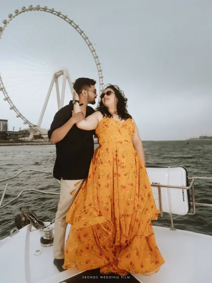 An intimate moment between the couple on a yacht, with the Ain Dubai ferris wheel creating a stunning, graphic background for their love story.