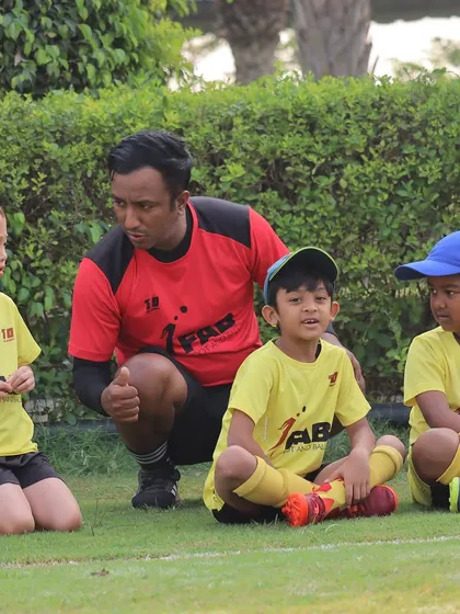 A coach kneels down to connect with his players at their level. This image embodies our approach of fostering skill development, resilience, and a deep love for the game through supportive coaching.