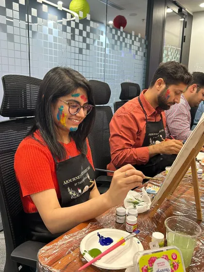 A smiling participant with paint on her face, fully embracing the messy, fun process of a Holi-themed workshop.